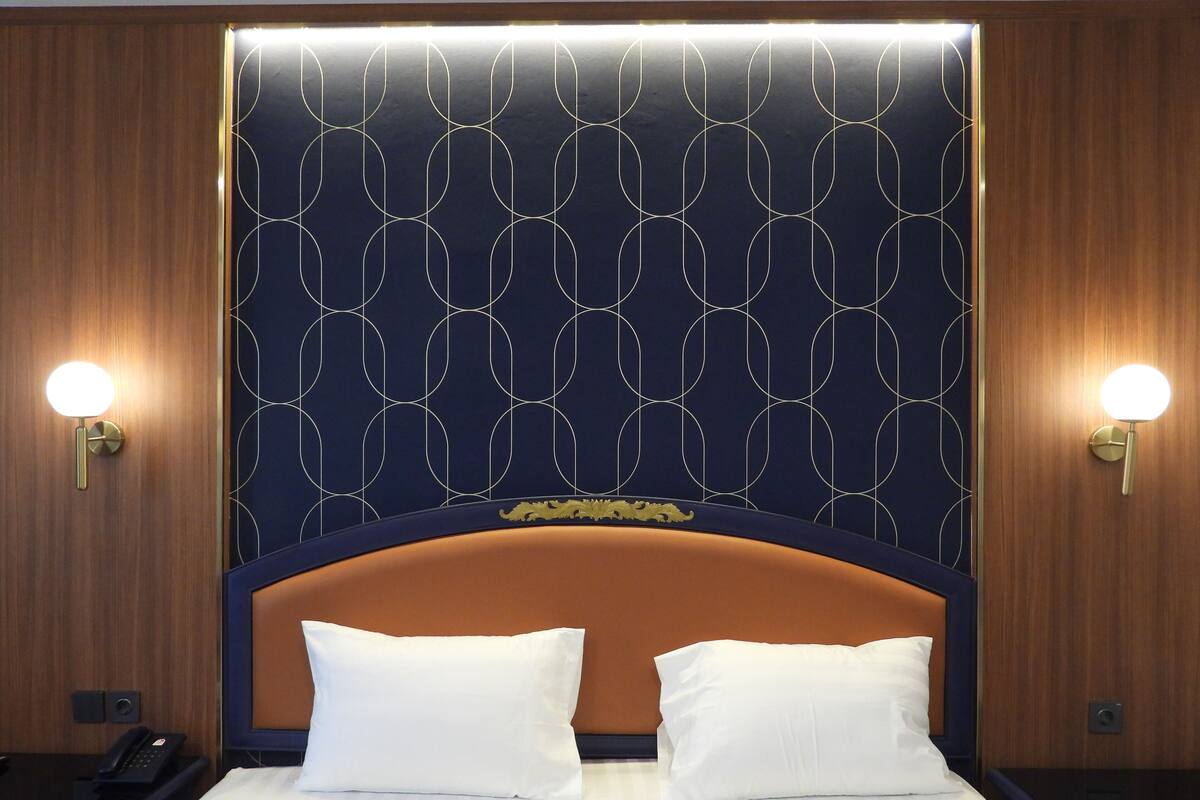 A hotel room with a large bed, two bedside lamps, and a patterned headboard.