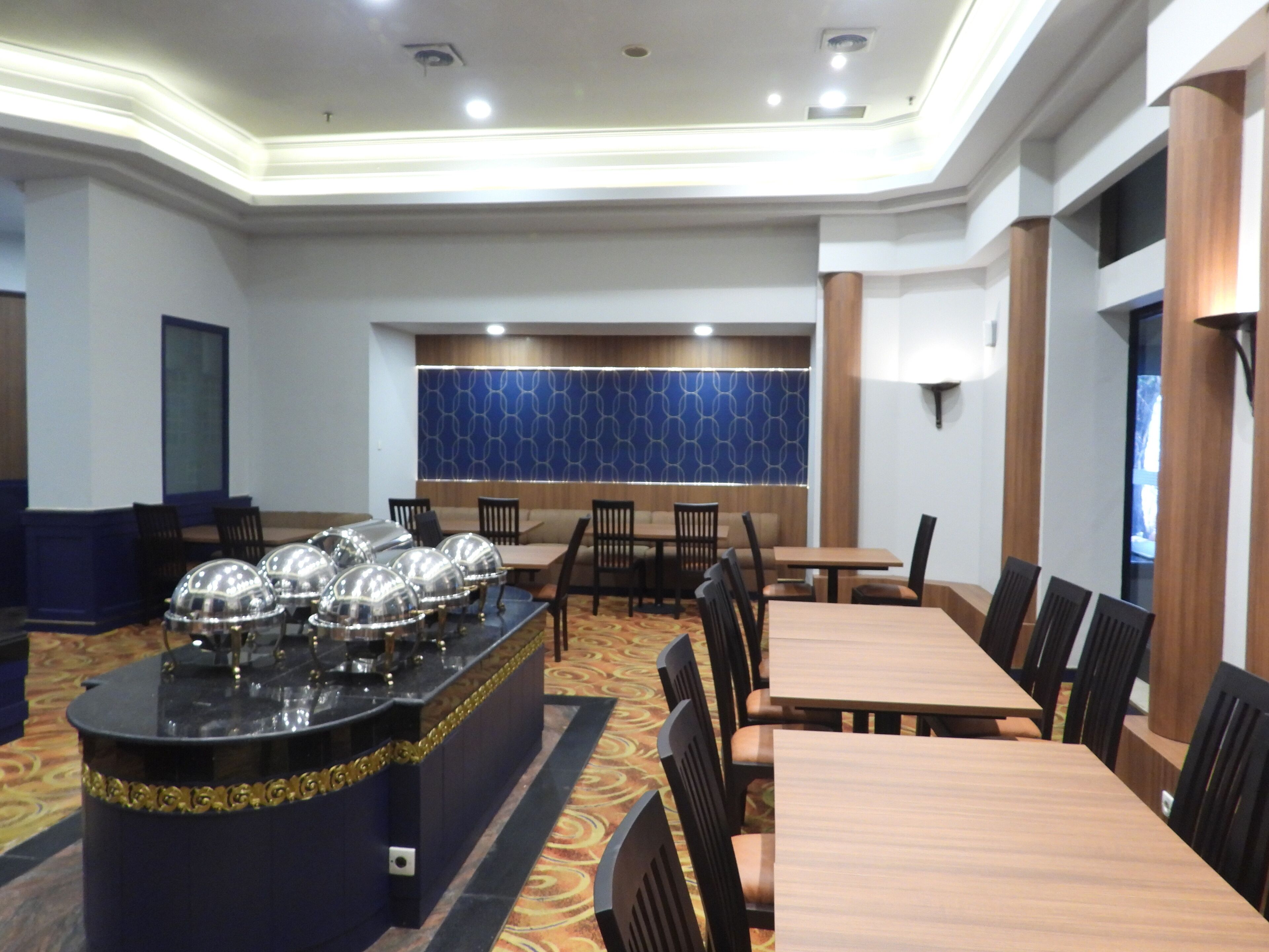 A hotel dining area with a buffet setup, multiple tables, and chairs.