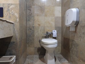 A bathroom with a toilet, a hand dryer, and a soap dispenser.