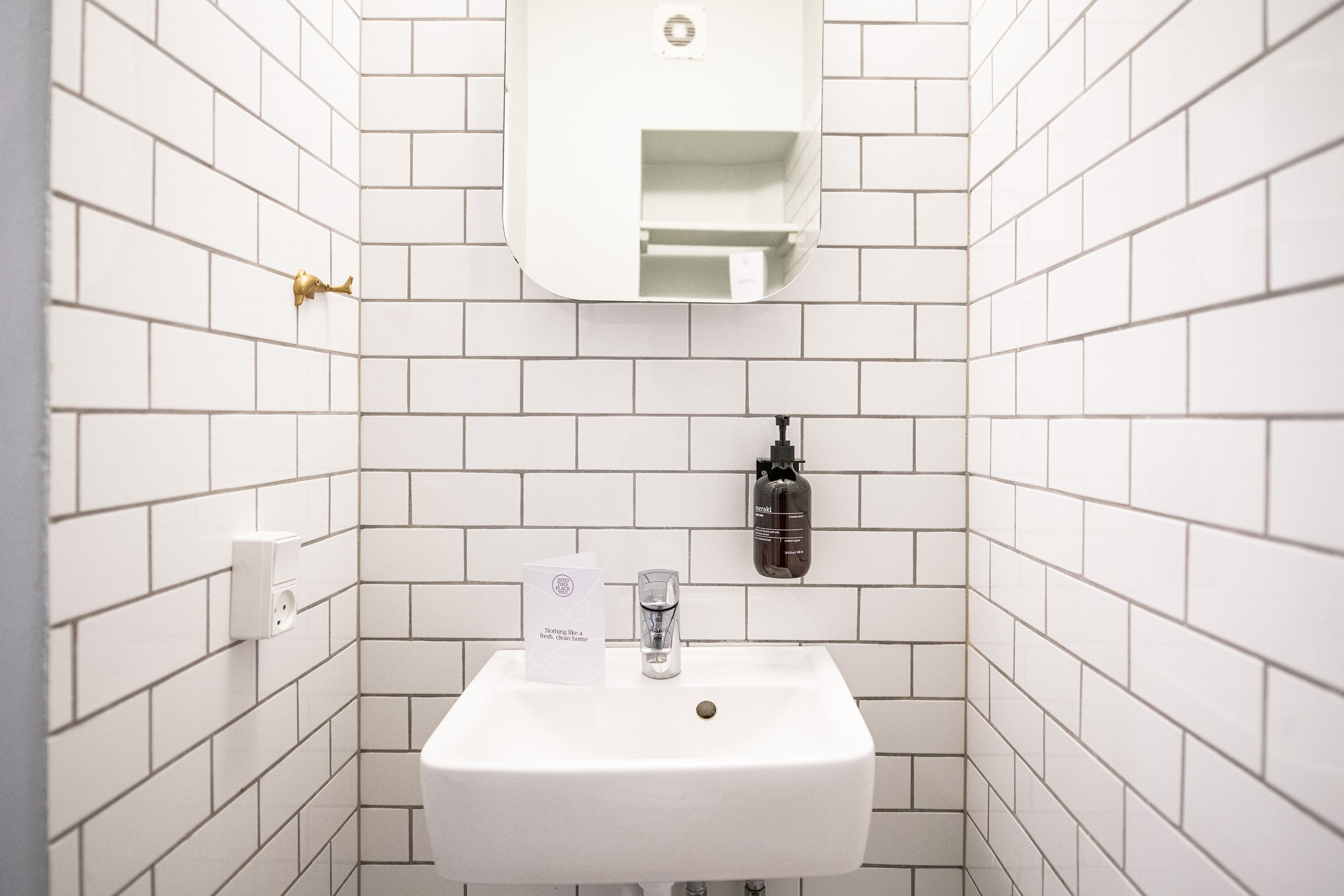 Een witte betegelde badkamer met een wastafel, een zeepdispenser en een papieren handdoekdispenser.