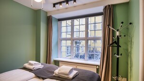 A hotel room with two beds, a window with a view of buildings, a coat rack, and a radiator. - Churchill 3BR by Daniel&Jacob's (Copenhagen)