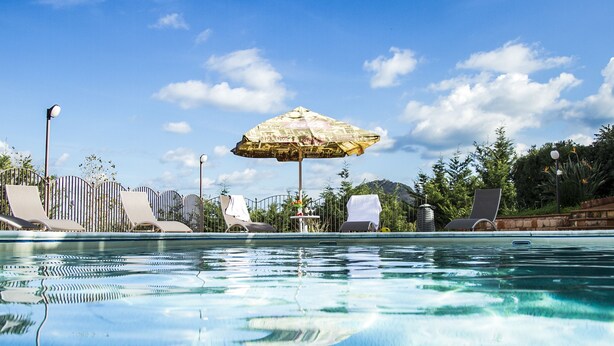 A swimming pool with lounge chairs and an umbrella, surrounded by greenery and a clear sky. - Residence Villa Santa Lucia (Cefalù)