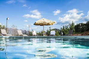 A swimming pool with lounge chairs and an umbrella, surrounded by greenery and a clear sky. - Residence Villa Santa Lucia (Cefalù)