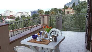 Un balcón con una mesa dispuesta para dos personas, una silla y vistas de la ciudad.