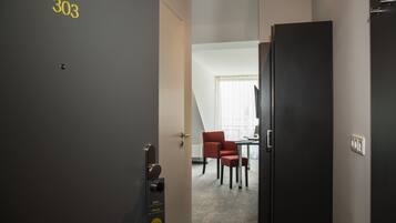 A hotel room with a door labeled '303', a desk, a chair, and a window with blinds.
