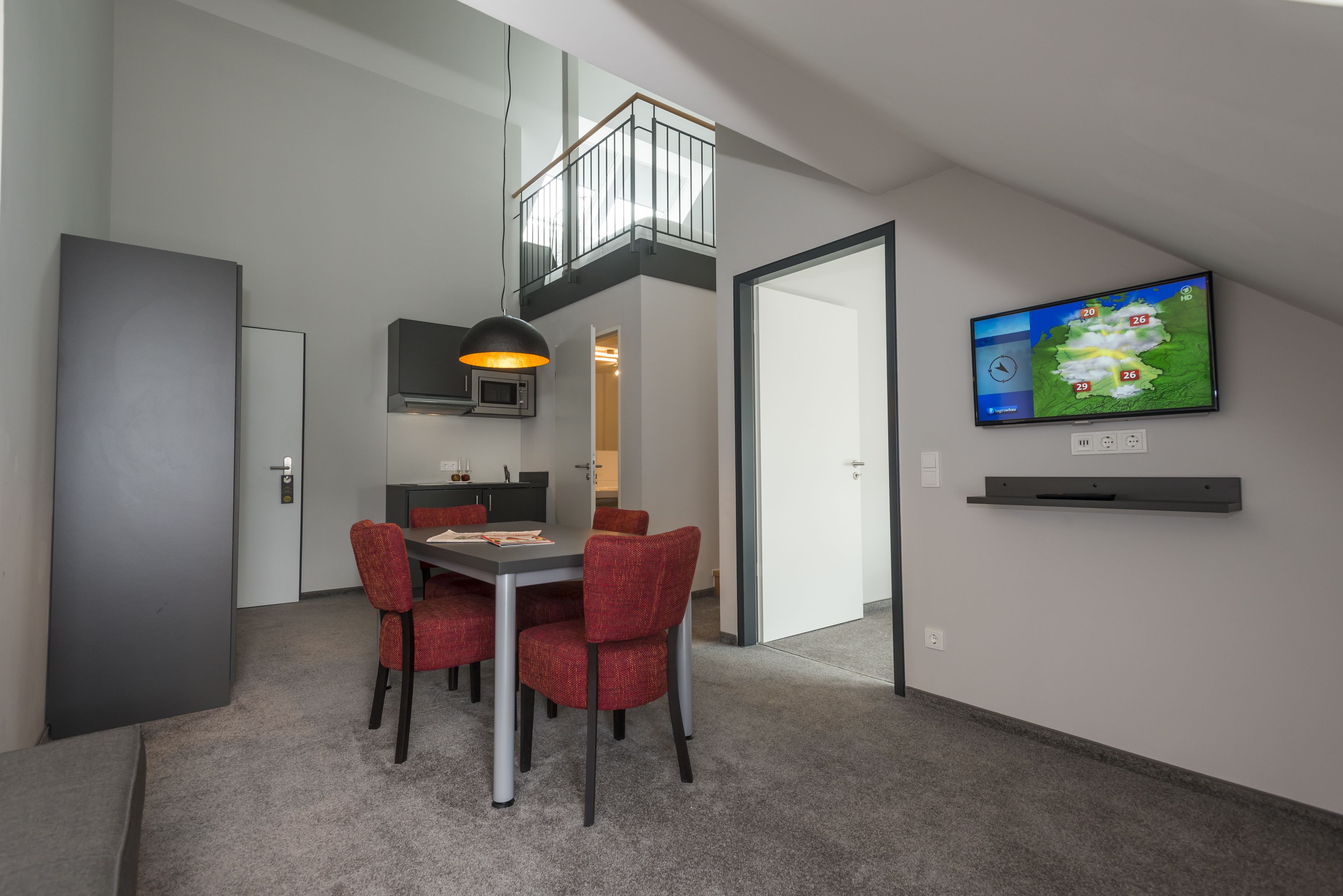 A modern dining area with a table and chairs, a television mounted on the wall, and a view of the cityscape.