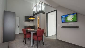 A modern dining area with a table and chairs, a television mounted on the wall, and a view of the cityscape.