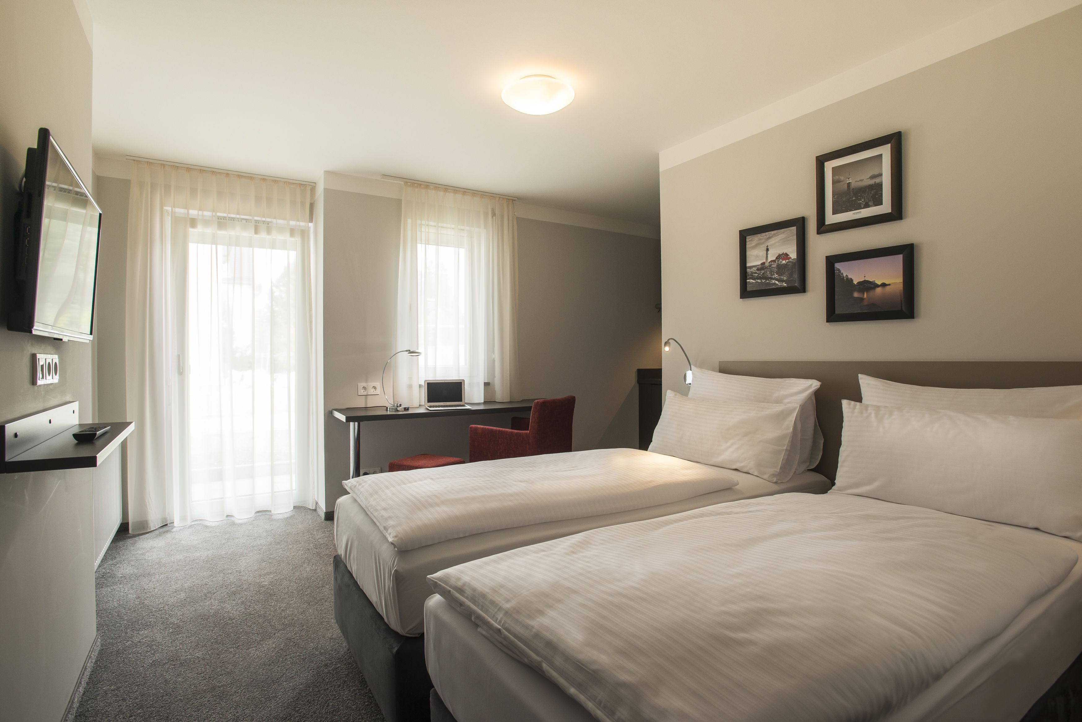 A hotel room with two beds, a desk with a chair, a TV, and three framed pictures on the wall.