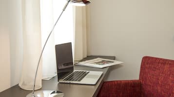 En bærbar computer på et skrivebord med en skrivebordslampe, en rød stol og et magasin.