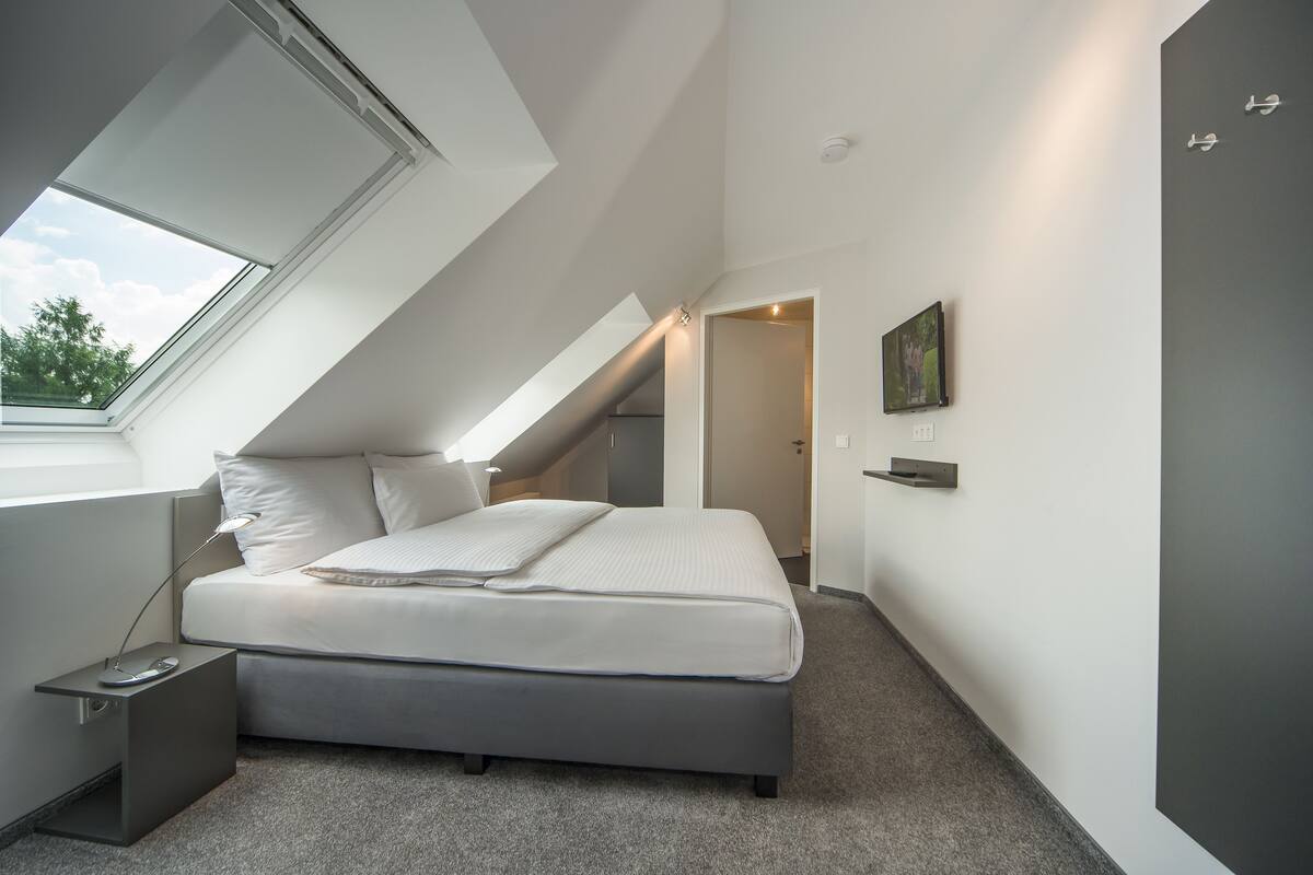 A modern bedroom with a skylight, a bed, a bedside table with a lamp, and a painting on the wall.