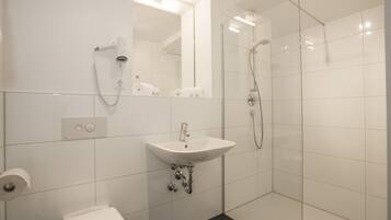 Een moderne badkamer met een witte wastafel, een toilet en een douchecabine met glazen wanden.