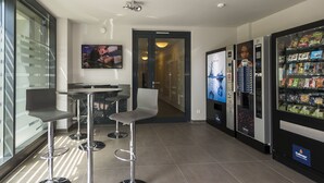A modern hotel lobby with a bar area, a television, vending machines, and a glass wall. - the Stay.residence (Planegg)