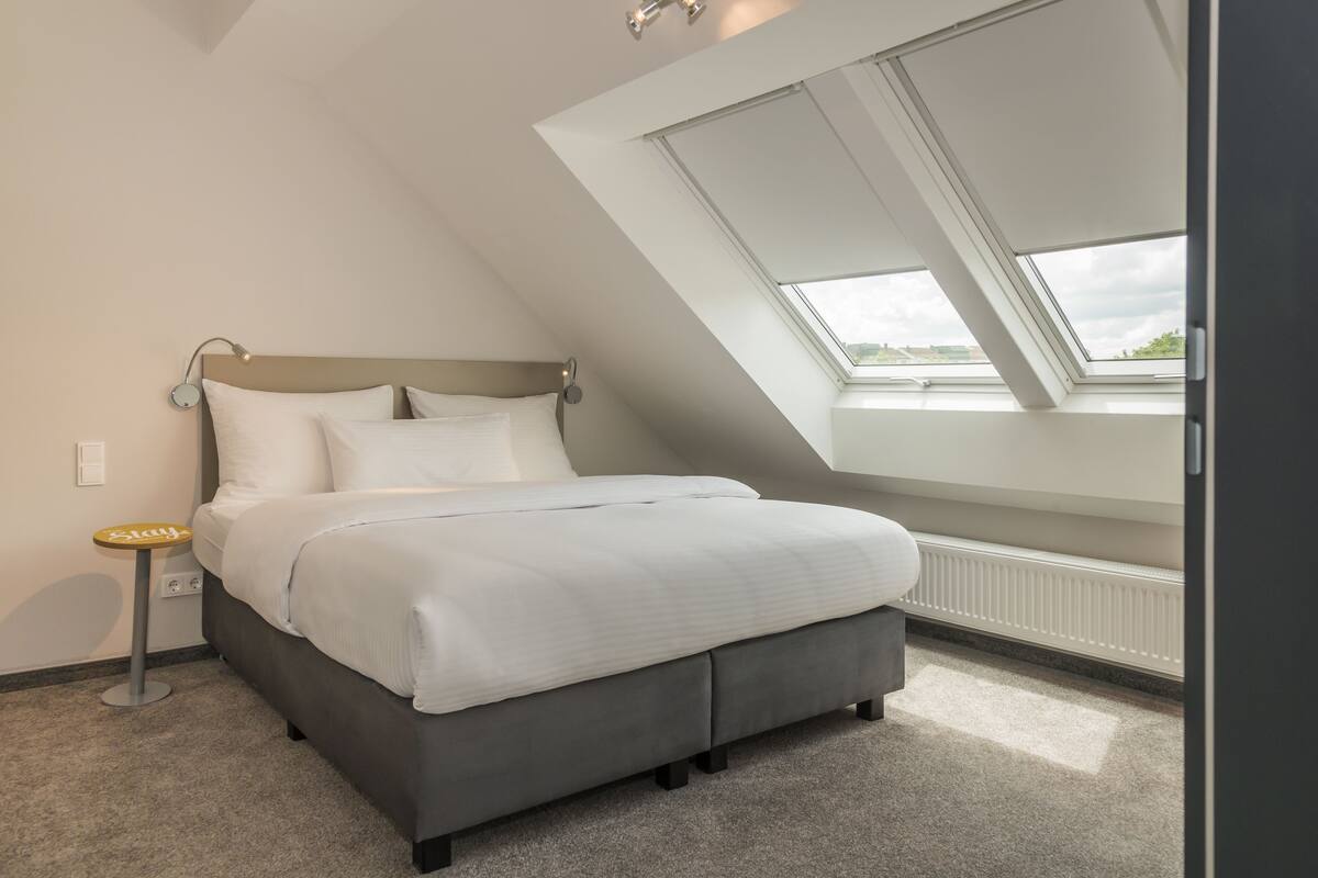 A bedroom with a bed, a bedside table, a skylight, and a radiator.