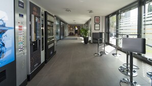 A modern hotel corridor with vending machines, a reception desk, and seating areas. - the Stay.residence (Planegg)
