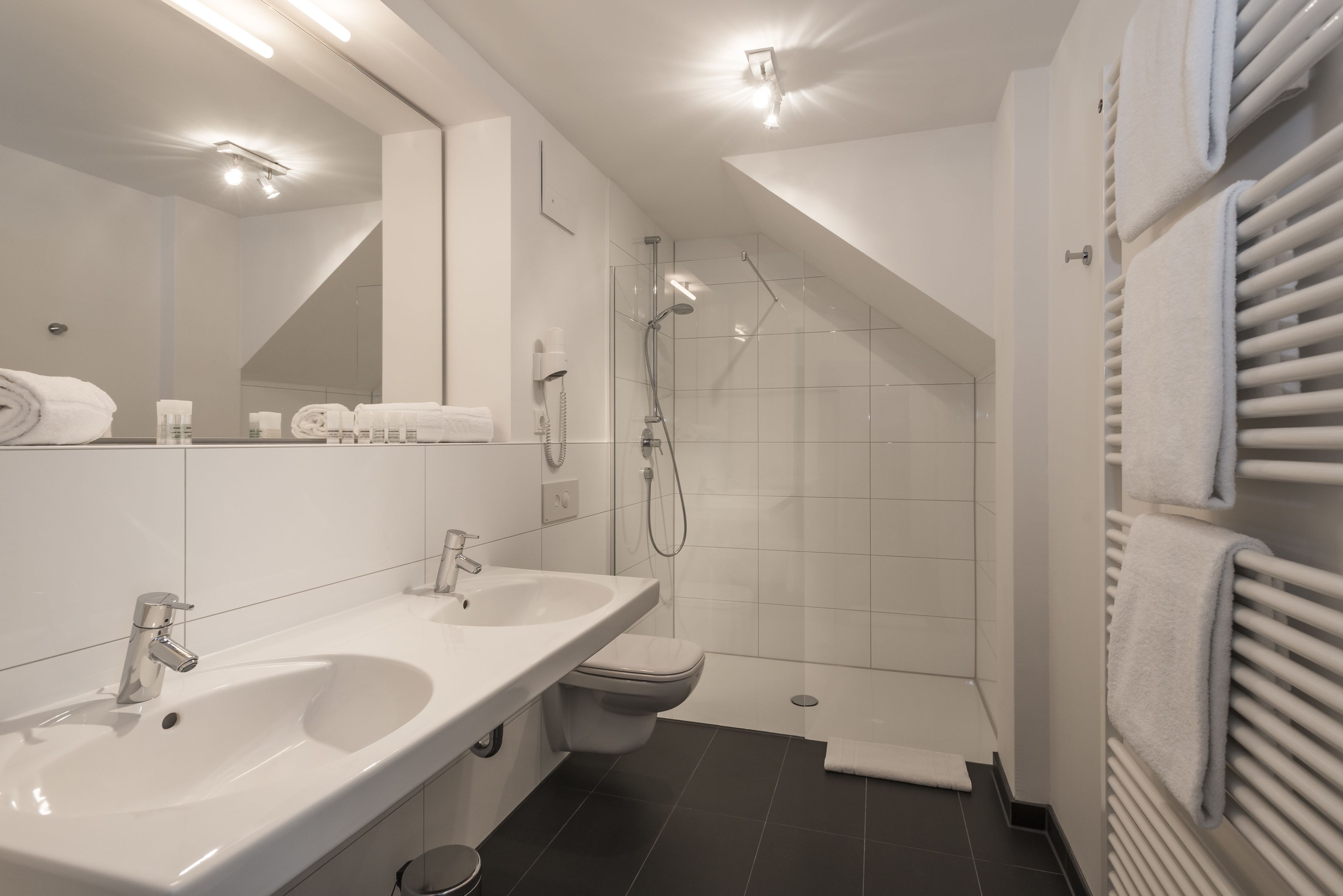 Et moderne badeværelse med stor vask, spejl, bruser og toilet.