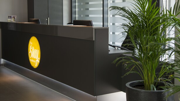 A reception desk with a 'Stay' sign, a potted plant, and a modern interior design. - the Stay.residence (Planegg)