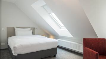 Een slaapkamer met dakraam, een bed, een rode stoel en een radiator.