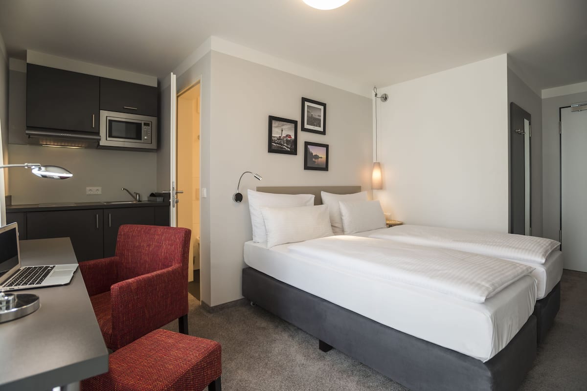 A hotel room with a bed, a desk with a laptop, a chair, a microwave, and a small kitchenette.