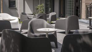 A modern outdoor seating area with contemporary chairs and tables, a small plant, and a building with large windows and a brick facade. - the Stay.residence (Planegg)