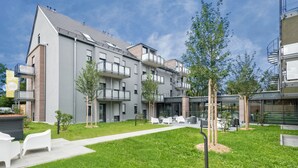 A modern apartment building with multiple balconies, a well-maintained lawn, and outdoor seating area. - the Stay.residence (Planegg)