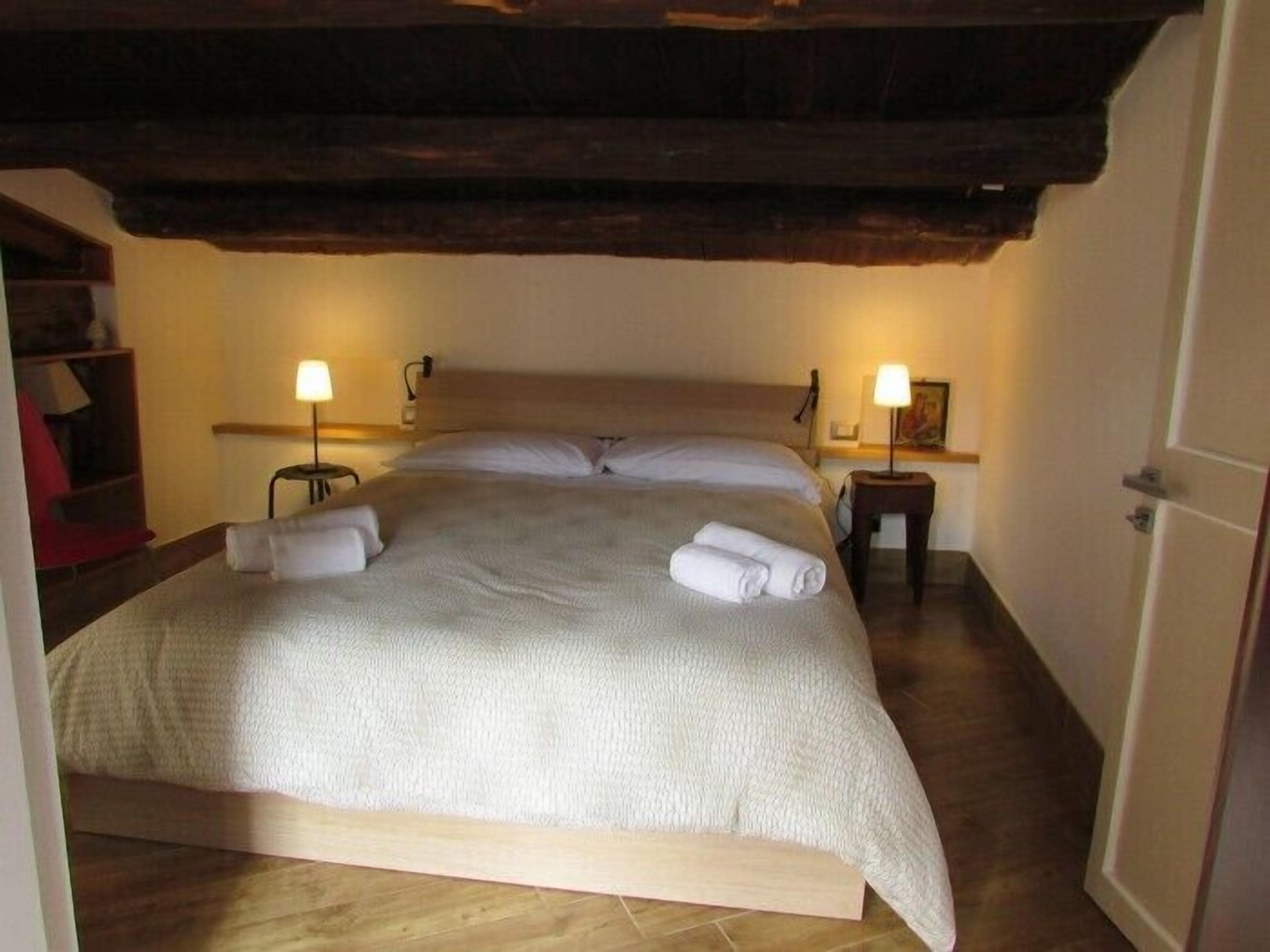 A neatly made bed with two pillows and two rolled towels, two bedside lamps, and a wooden headboard.