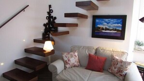 Ein modernes Wohnzimmer mit einem beigefarbenen Sofa, einer Treppe mit Holzdielen und einem gerahmten Landschaftsbild an der Wand.