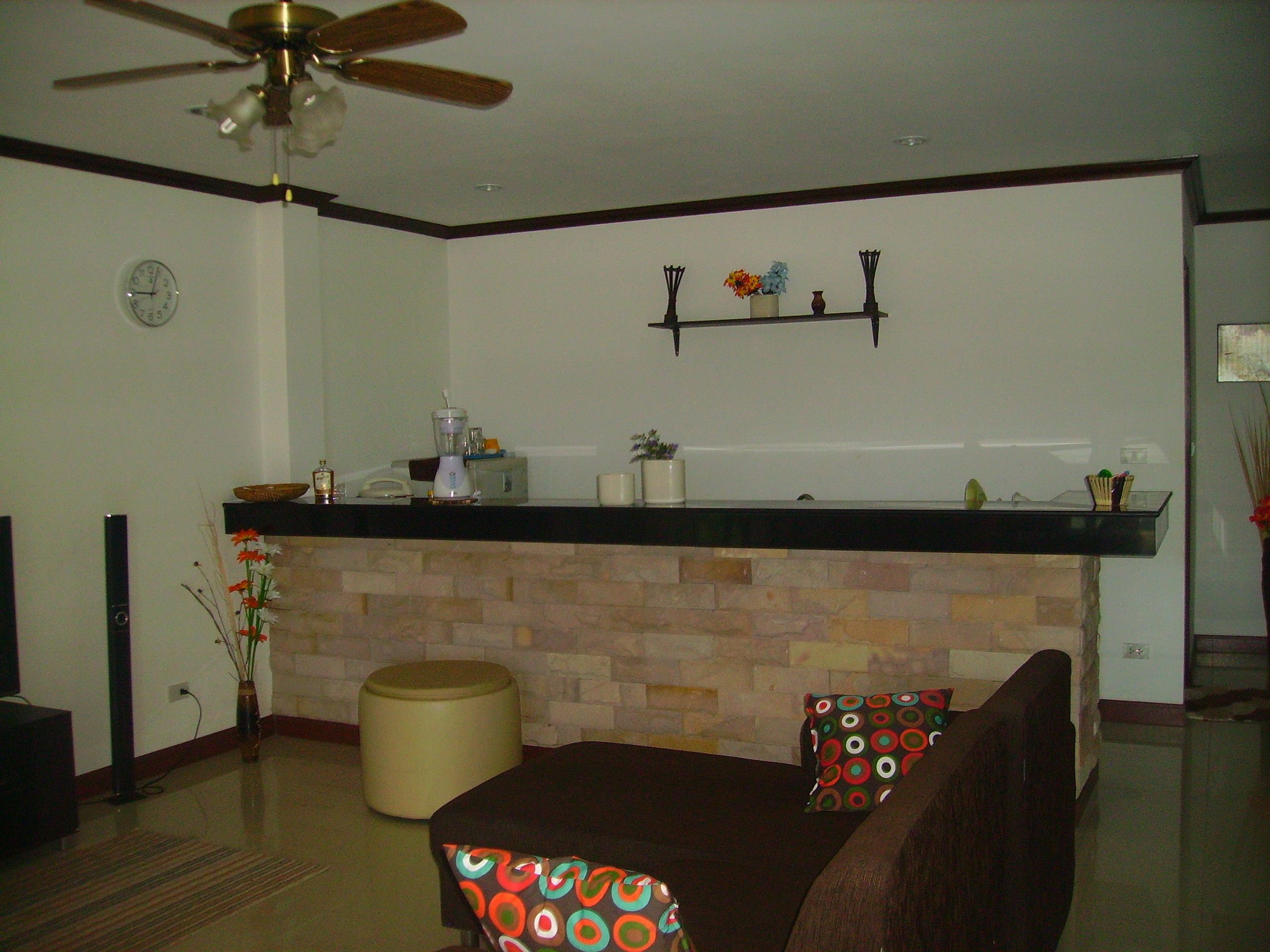Una sala de estar con chimenea, una mesa de comedor con cojines coloridos, un ventilador de techo y un reloj en la pared.