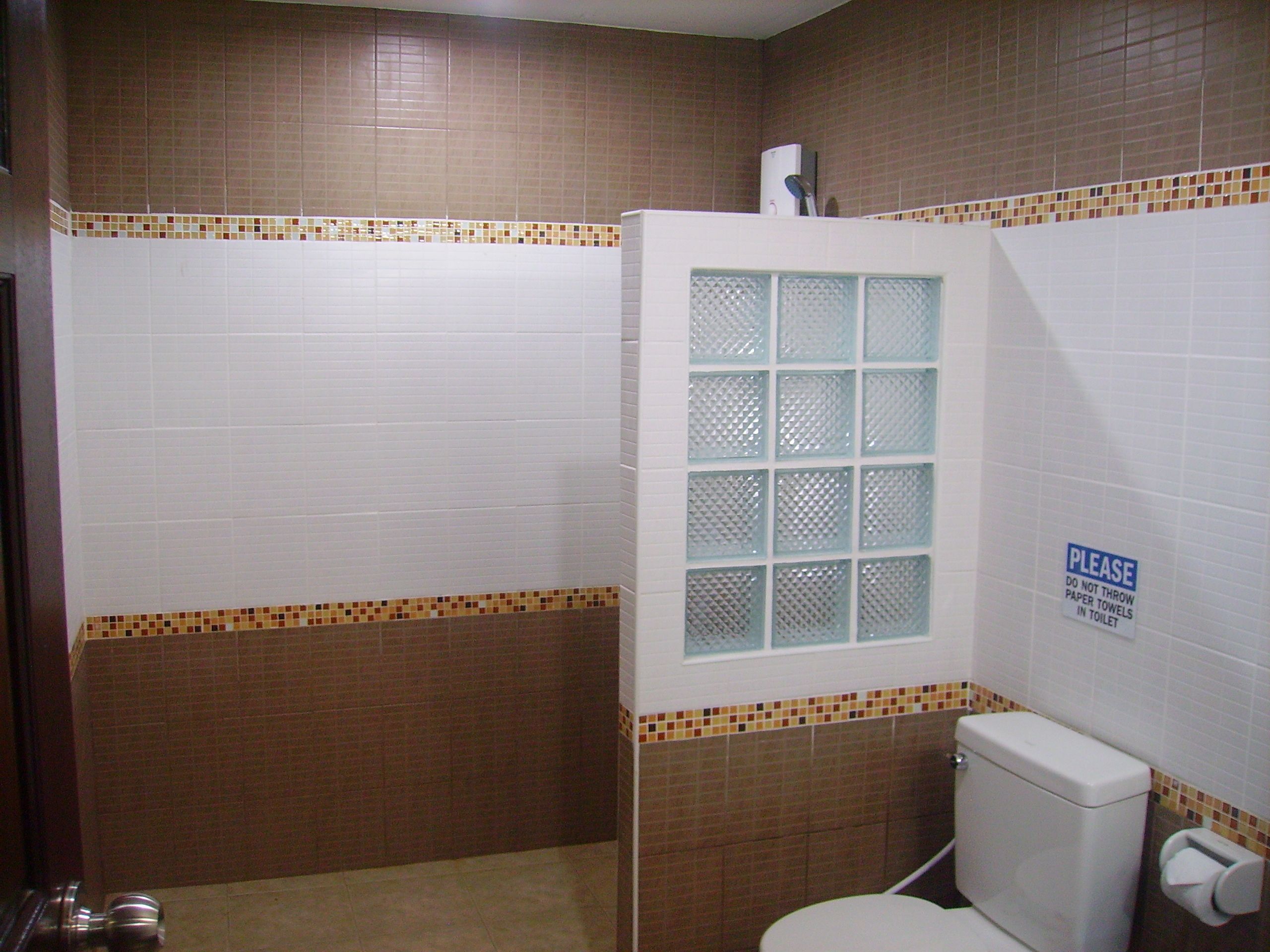 A bathroom with a shower, toilet, and a sign instructing not to throw paper towels in the toilet.