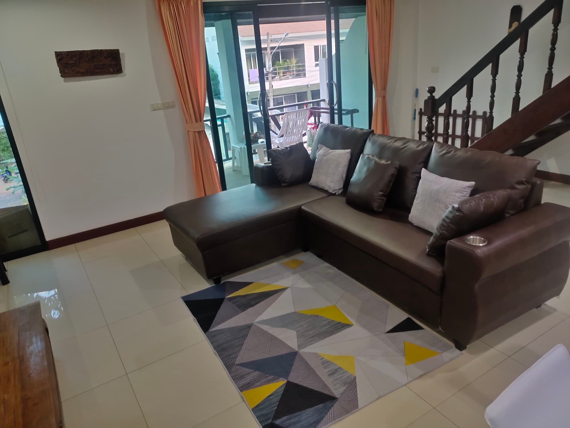 A living room with a sectional sofa, a geometric rug, and a staircase.
