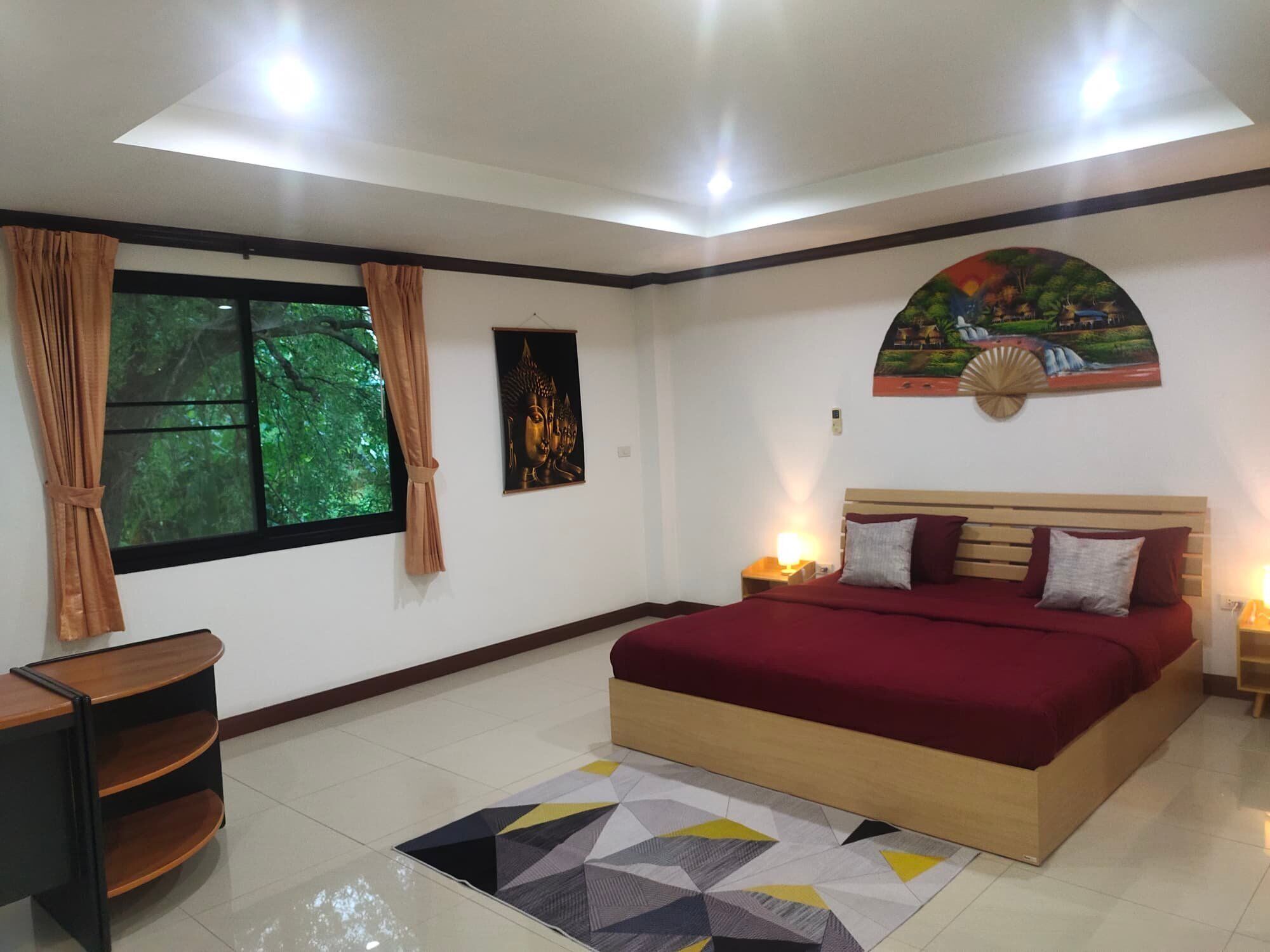 Quarto com uma cama grande, mesa de cabeceira, escrivaninha e janela com cortinas.