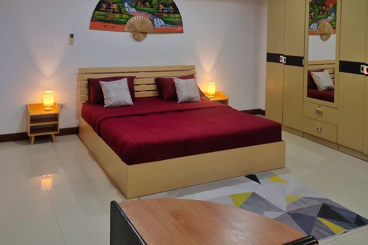 Un dormitorio con cama, lámparas de noche, mesita de madera, espejo y luz de techo.