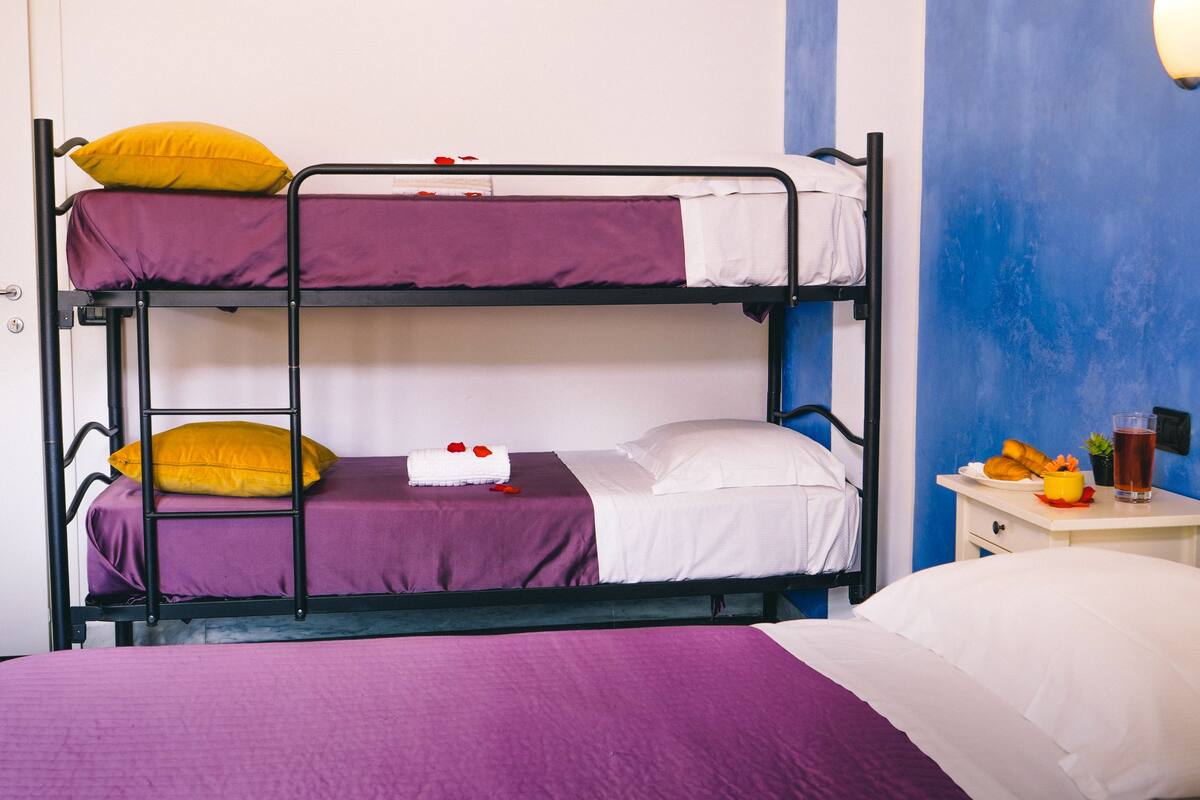 A bunk bed with purple bedding, a small table with a drink and snacks, and a blue wall.