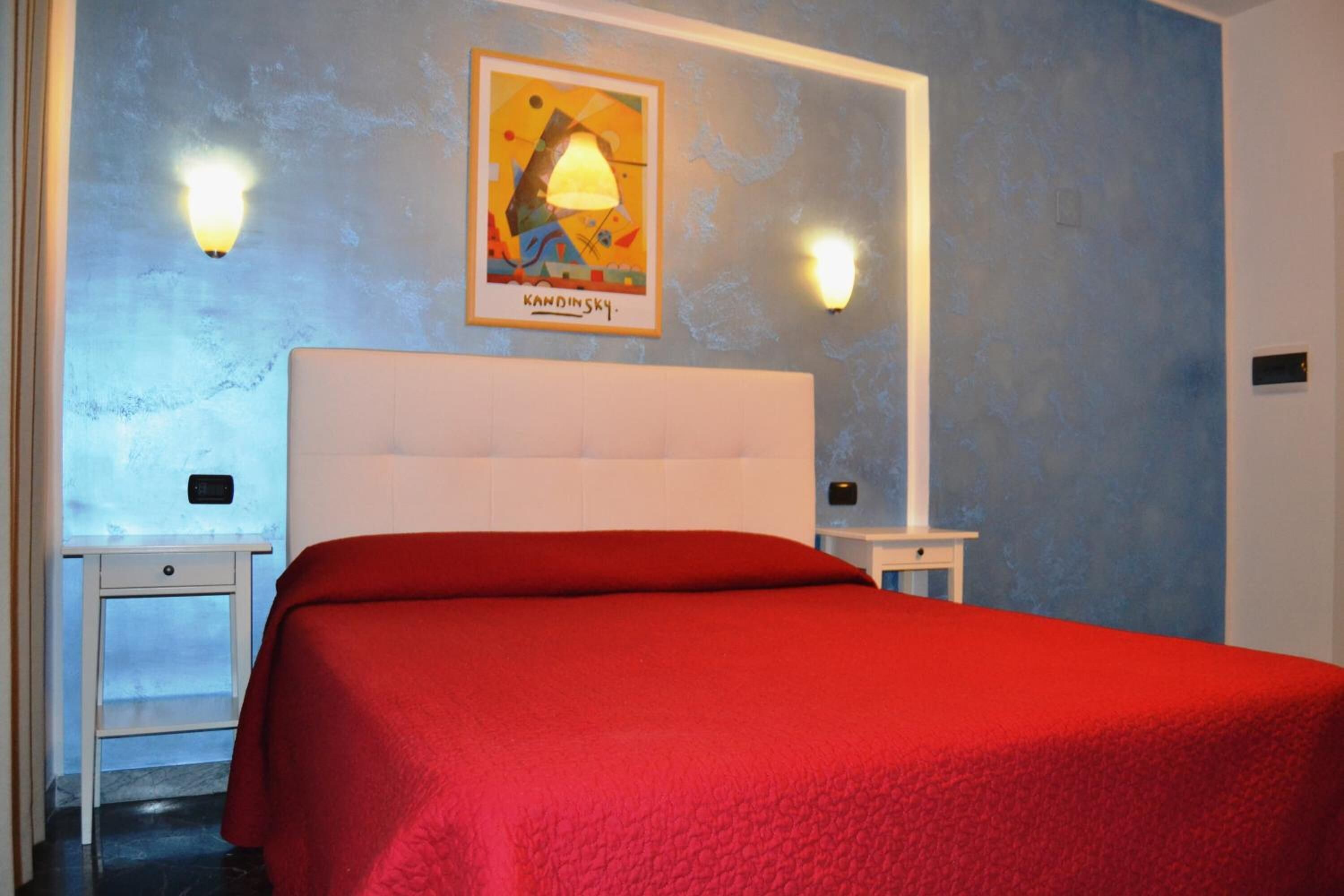 A hotel room with a red bedspread, a white headboard, and two bedside tables.