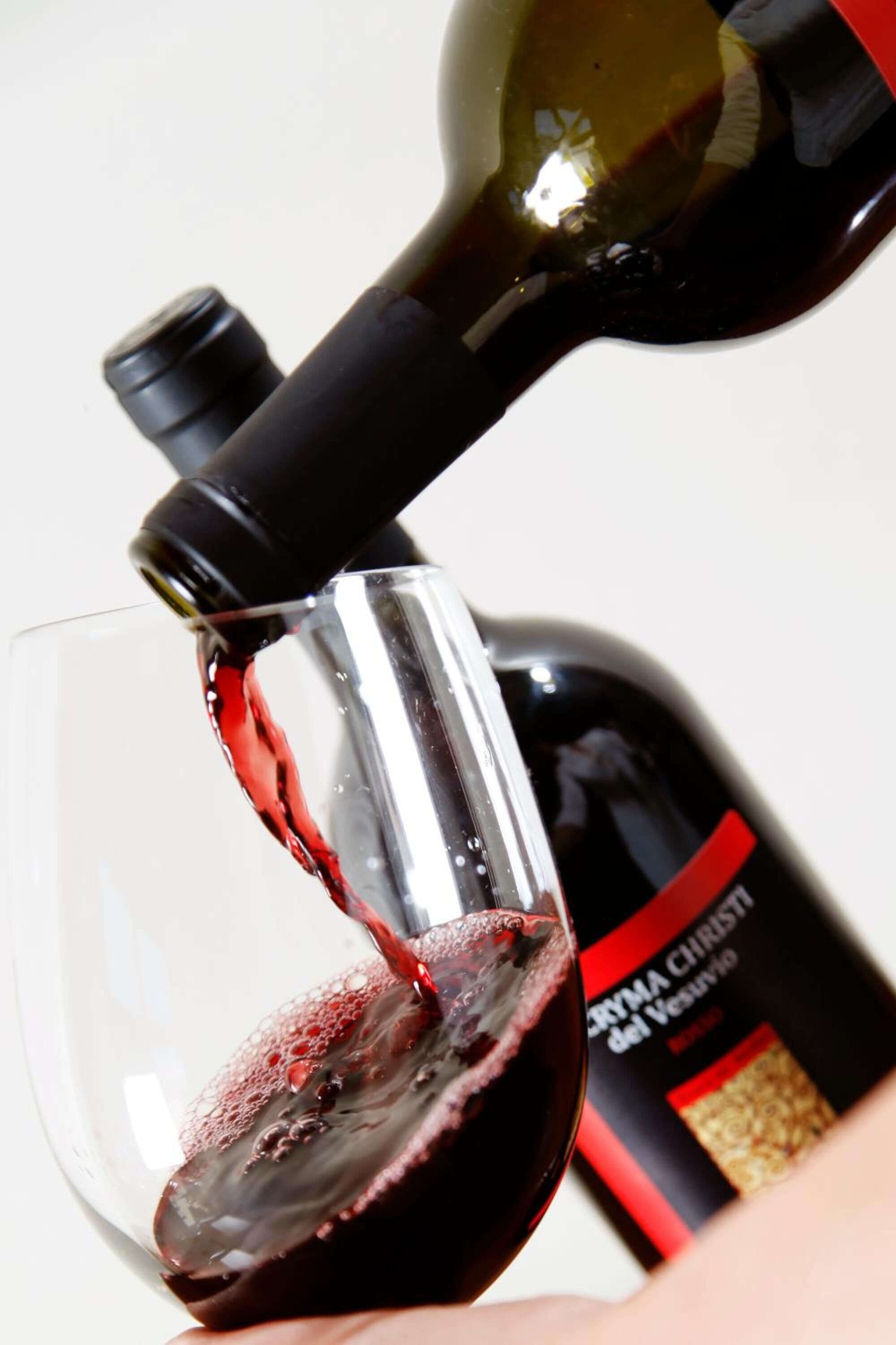 A wine bottle pouring red wine into a glass.