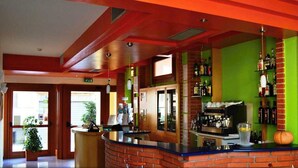 Zona de bar con mostrador, estanterías llenas de botellas y una pared verde.