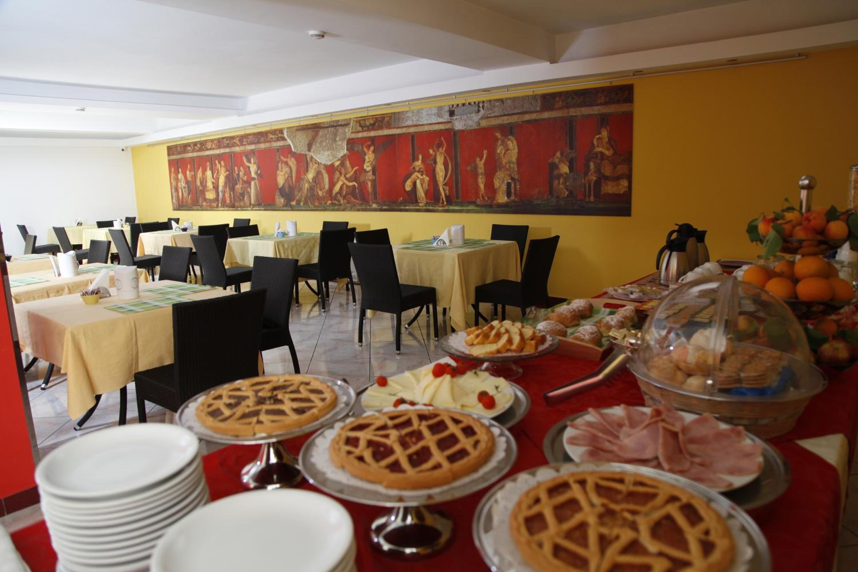 A dining area with tables set for breakfast, featuring pastries, fruits, and a variety of dishes.