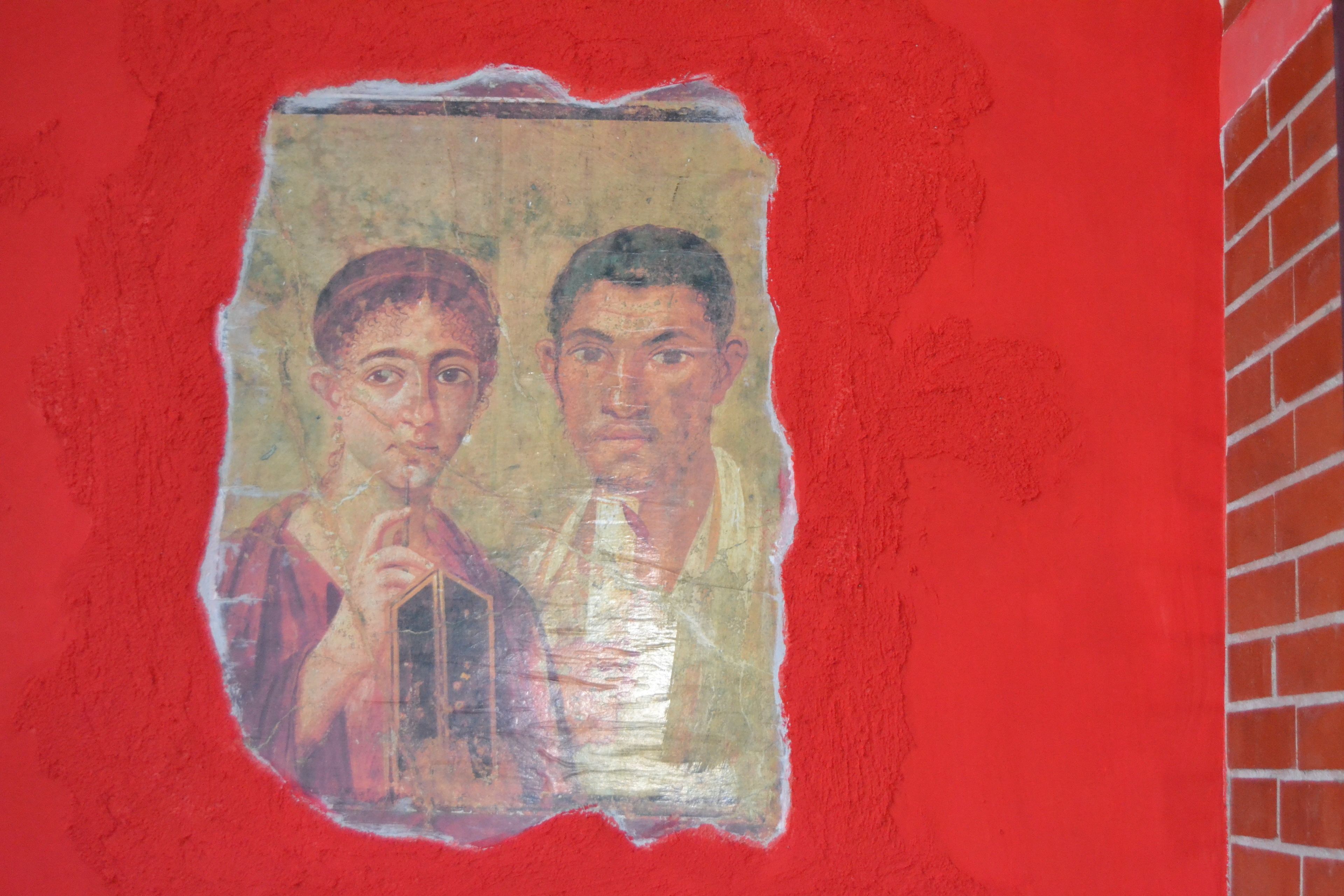 Un mur rouge orné d’une fresque délavée représentant deux personnages.