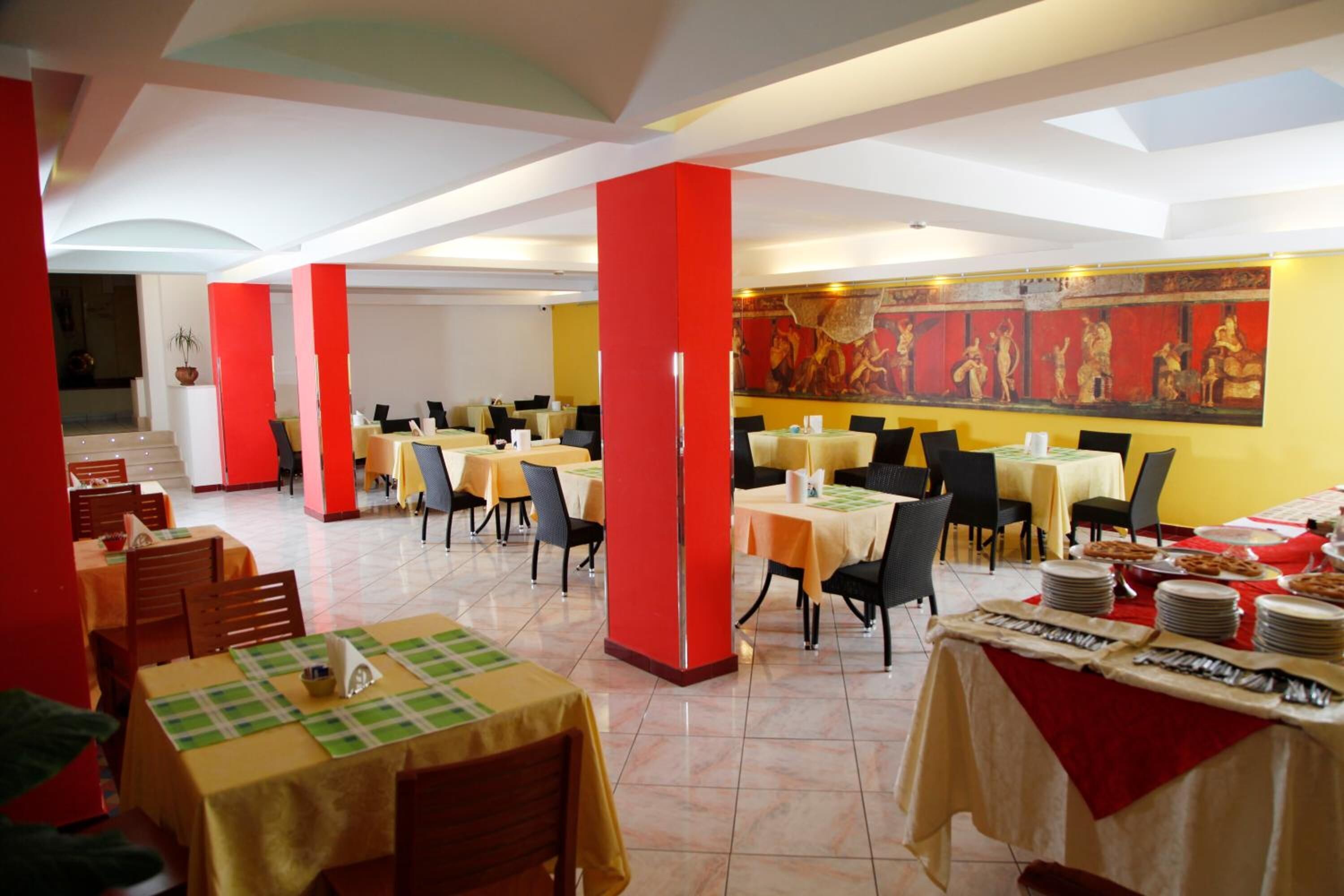 A restaurant with multiple tables, red pillars, and a mural on the wall.
