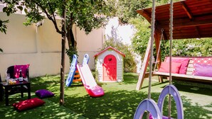Un patio trasero con área de juegos que incluye un tobogán, una casita roja y un conjunto de columpios.