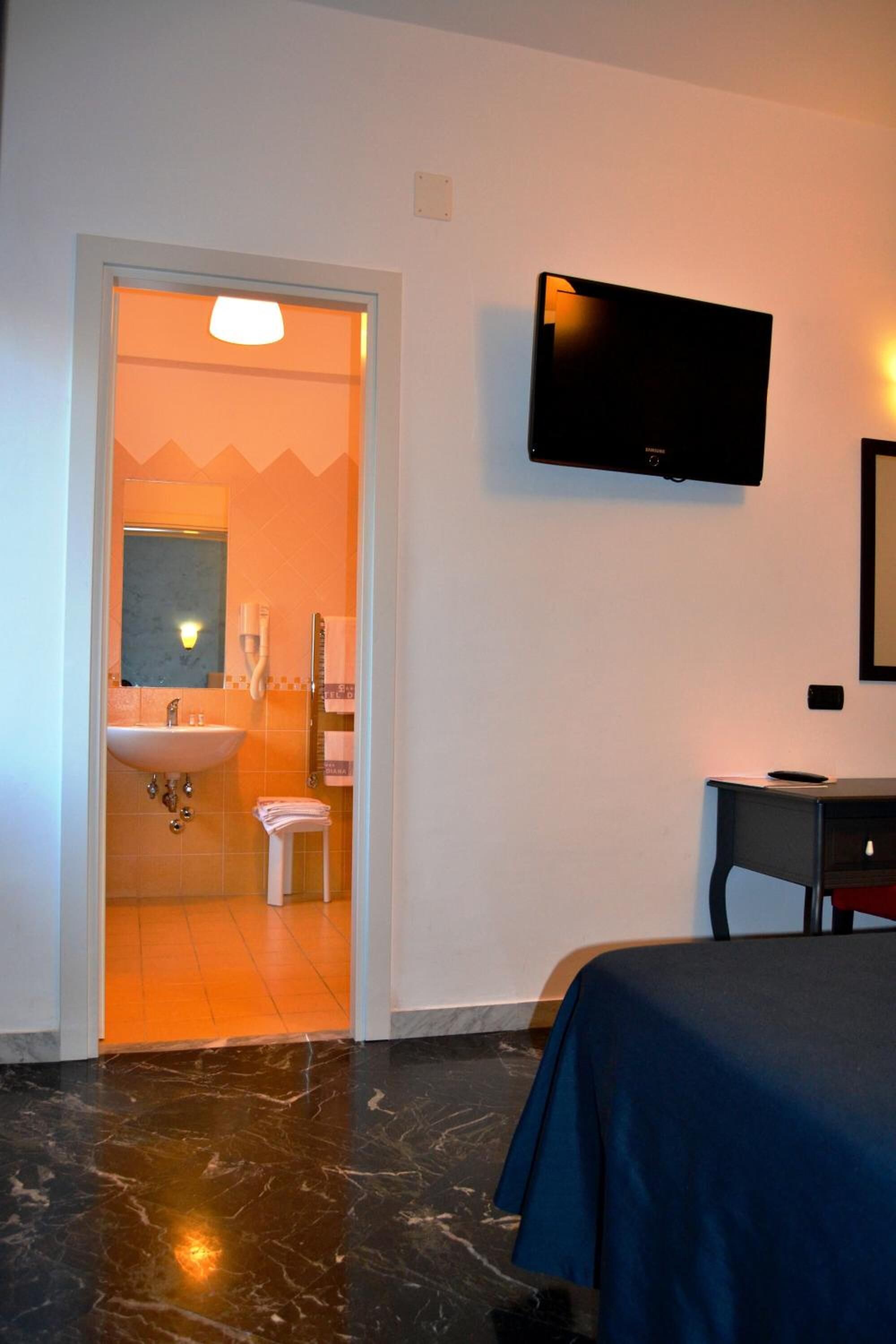 Habitación de hotel con cama, televisión montada en la pared, lavamanos y espejo en el baño.