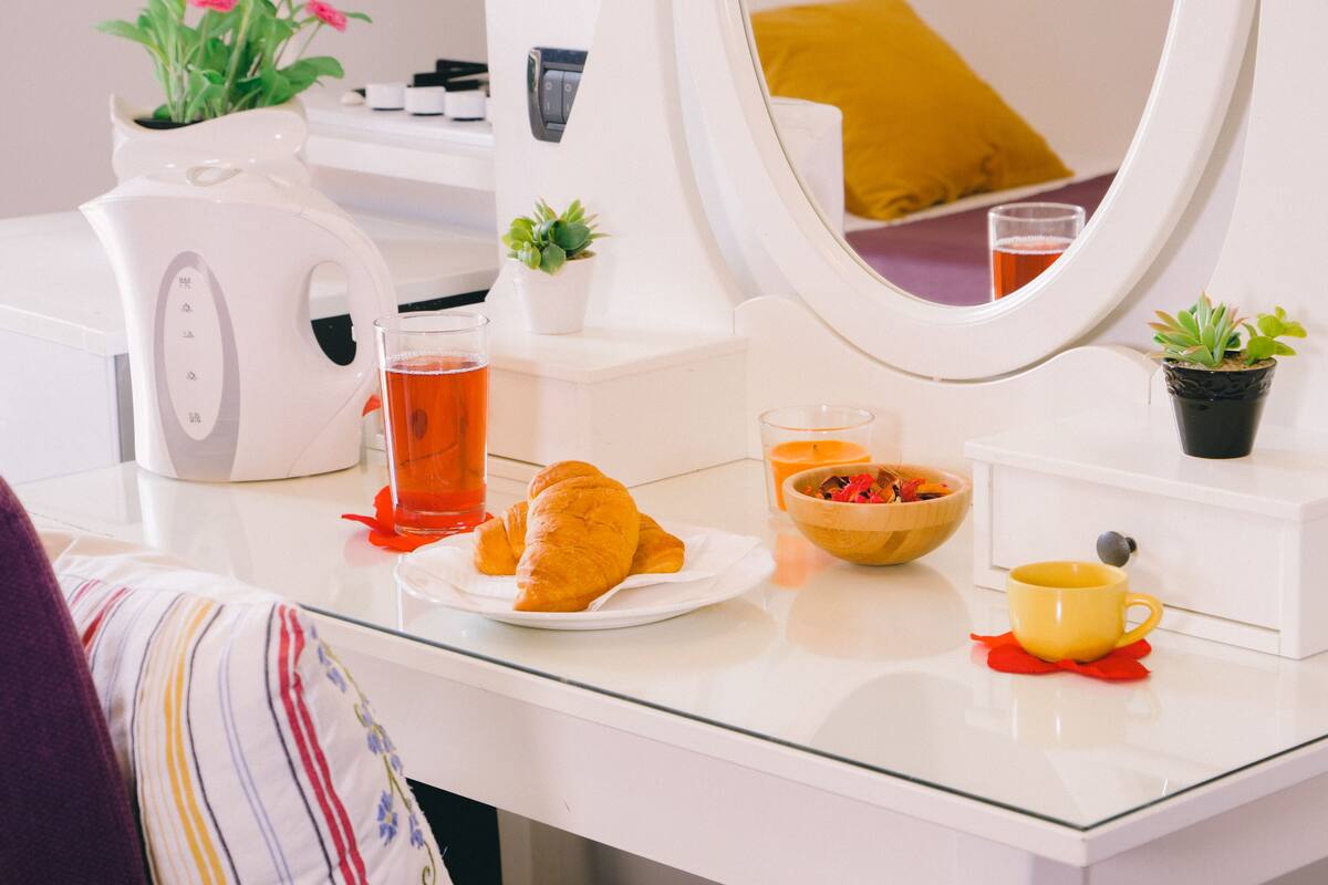 A breakfast setup with croissants, tea, and a bowl of fruit on a white countertop.