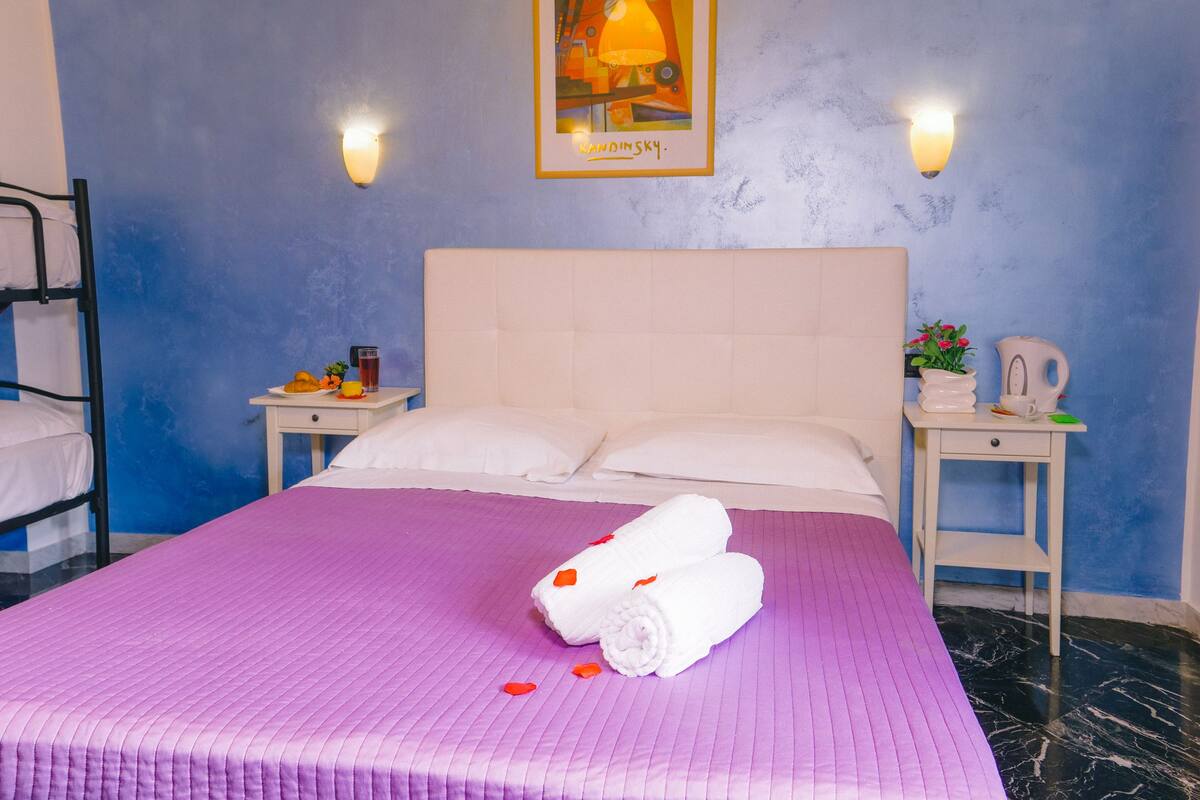 A hotel room with a bed, two bedside tables, a wall-mounted lamp, and a framed picture.