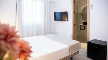 Een hotelkamer met een bed, een televisie aan de muur, een spiegel en een zwarte koffer op de vloer.