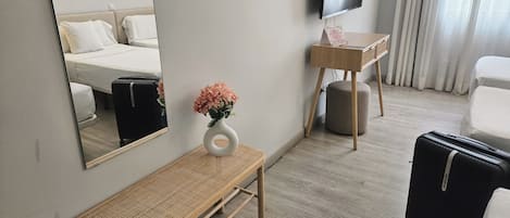 A hotel room with a bed, a desk with a TV, a bench, and a suitcase.