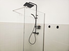 Een douche met glazen wand, een handdouche en een douchekop.