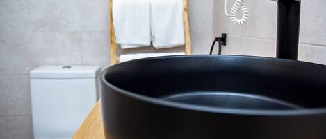 A modern bathroom with a black basin, white toilet, and a wooden counter.