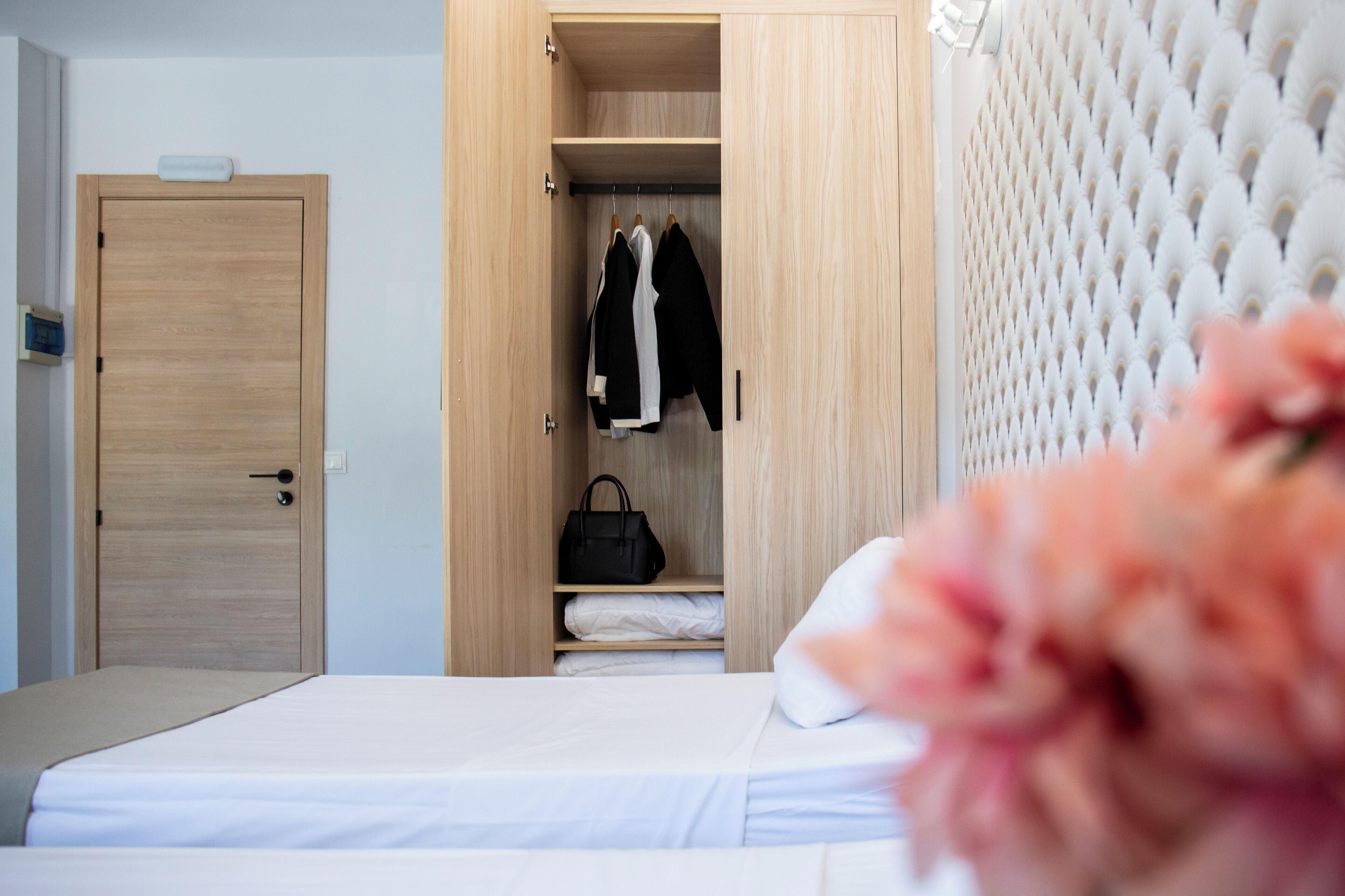 Habitación de hotel con un armario de madera, una cama con ropa blanca y una flor rosa en primer plano.