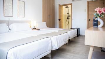 Habitación de hotel con dos camas, zona de ducha y un escritorio de madera con un jarrón de flores.