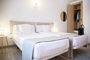 Een tweepersoonsbed met witte lakens, een nachtkastje, een houten garderobe en een ronde spiegel.