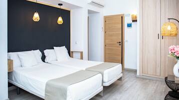 Une chambre d’hôtel moderne avec deux lits, une armoire en bois et une petite table sur laquelle est posé un vase.
